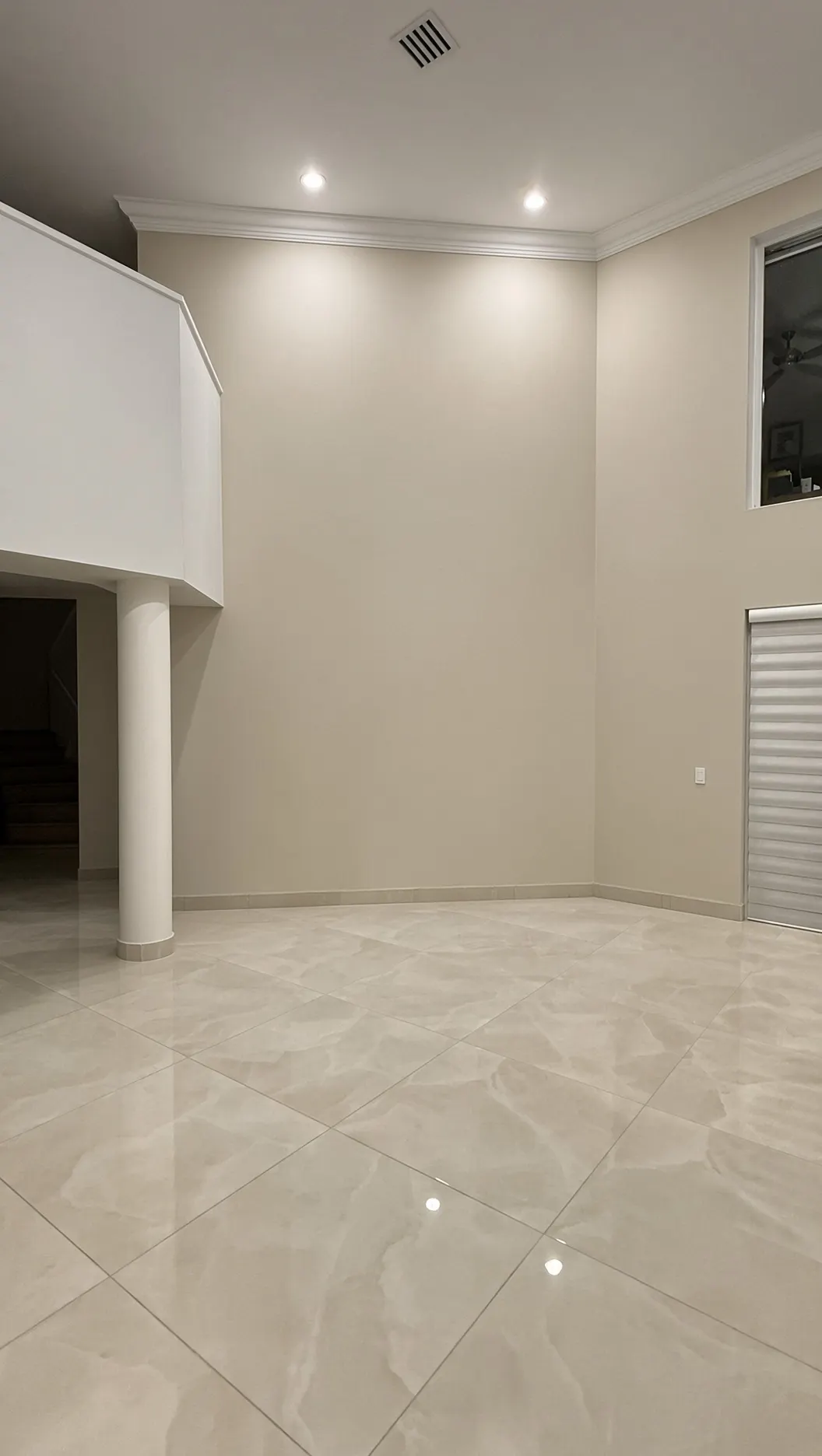 Double-height living room wall before: plain beige paint between a column and a window, with nothing on it
