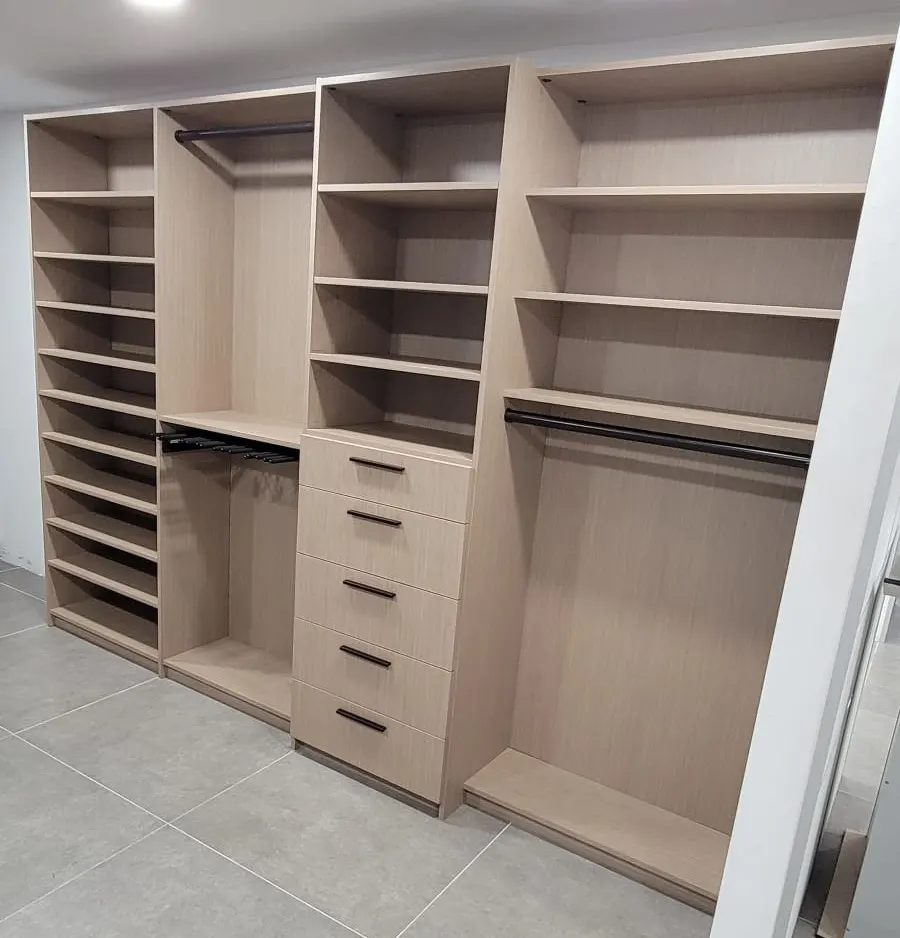 Light oak closet with a wall of shoe shelves, a pull-out trouser rack, five drawers and full-width hanging rails