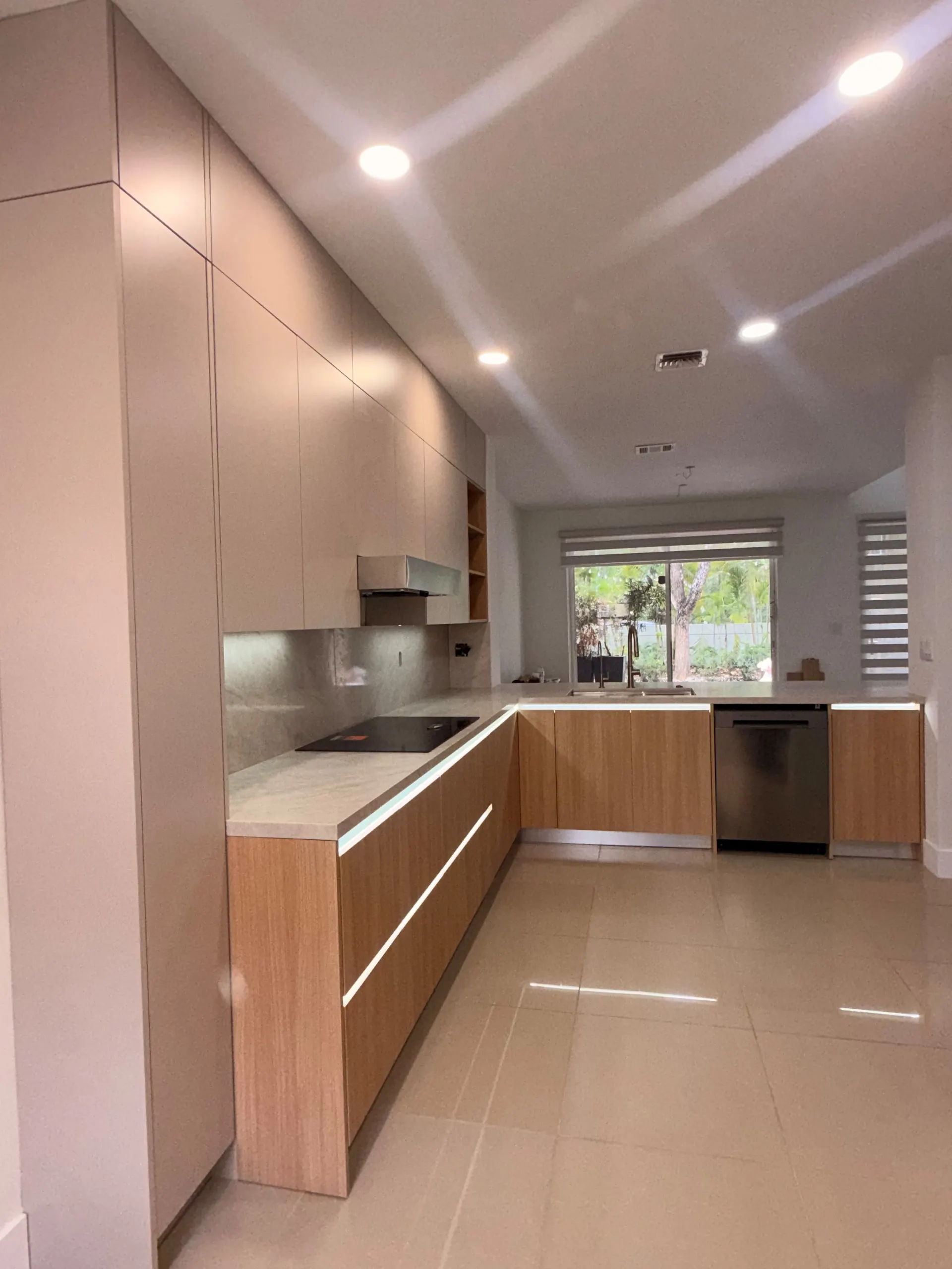 L-shaped kitchen with oak base cabinets, cream tall cabinets up to the ceiling and an LED strip under the marble counter edge