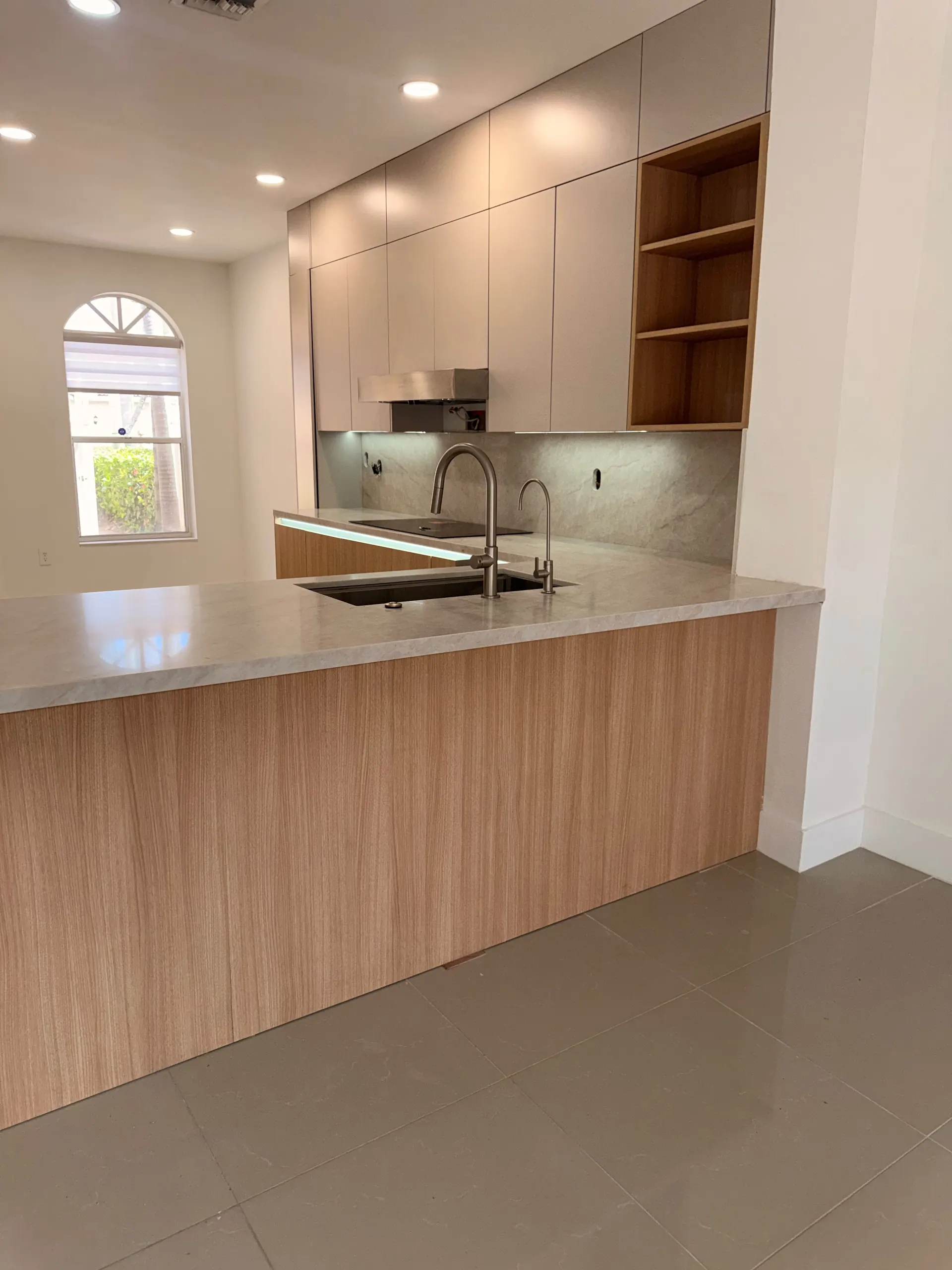 Kitchen peninsula in marble and oak facing the cooktop wall, with a stainless hood and open oak shelving