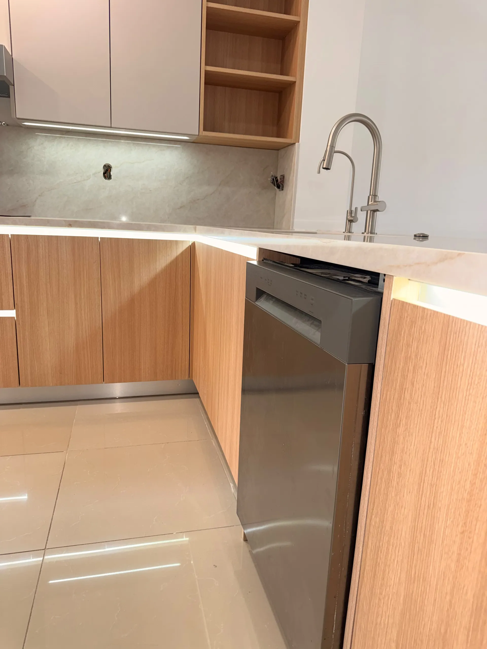Corner of the same kitchen, with the marble backsplash, the LED strip under the counter edge and the dishwasher panelled into the oak run