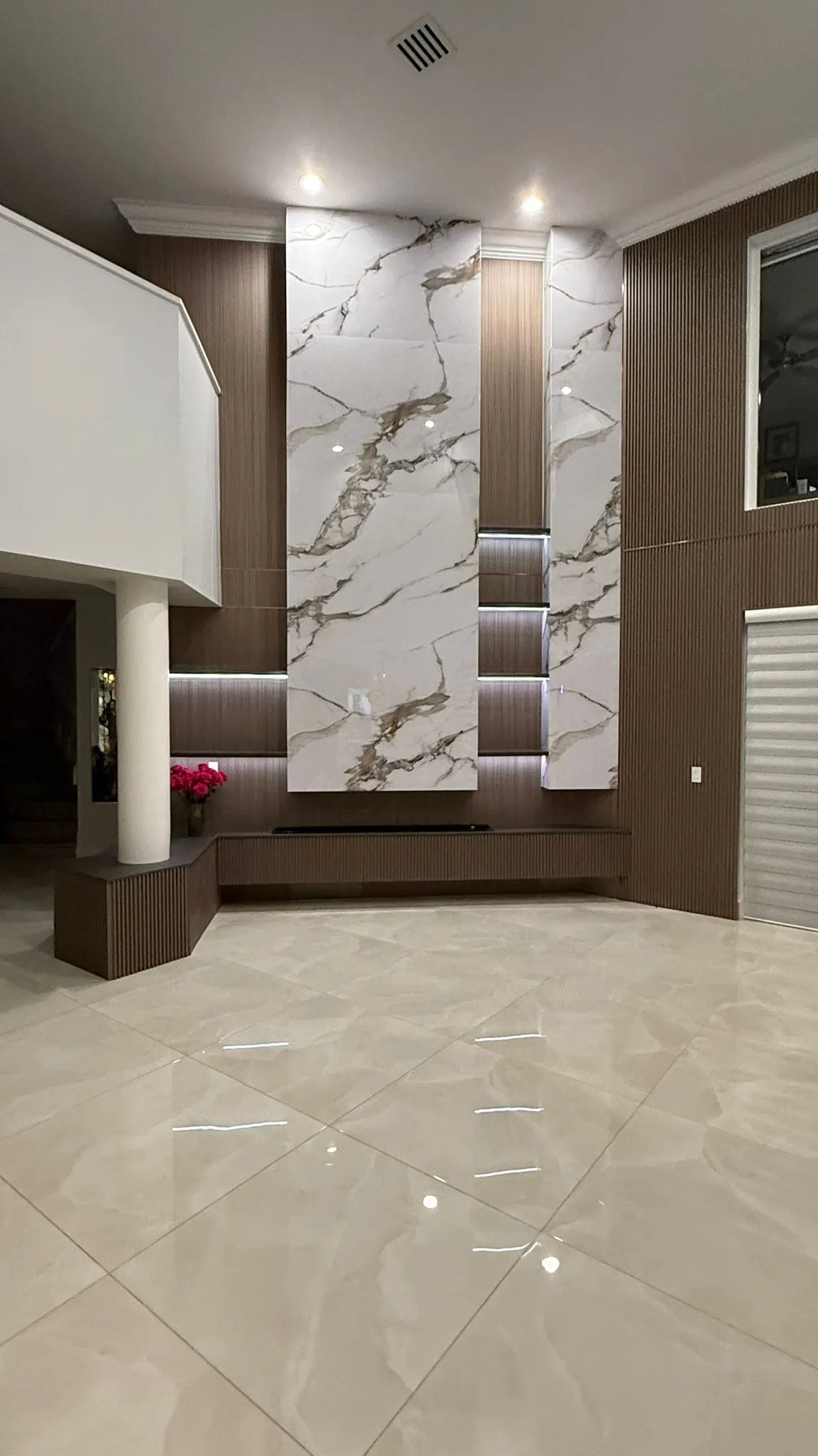 Double-height feature wall in marble-look panels and fluted wood, with lit niches and a low console